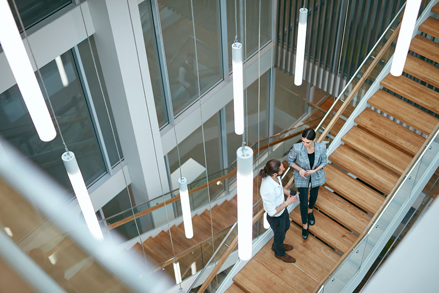 Why Go Independent - View of Two Coworkers Standing on a Wooden Staircase in a Modern Office Building While Talking